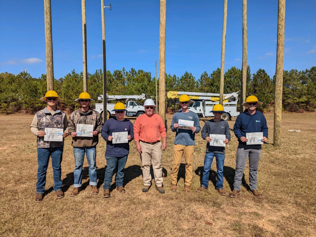 lineman graduates standing with certificates and hardhats