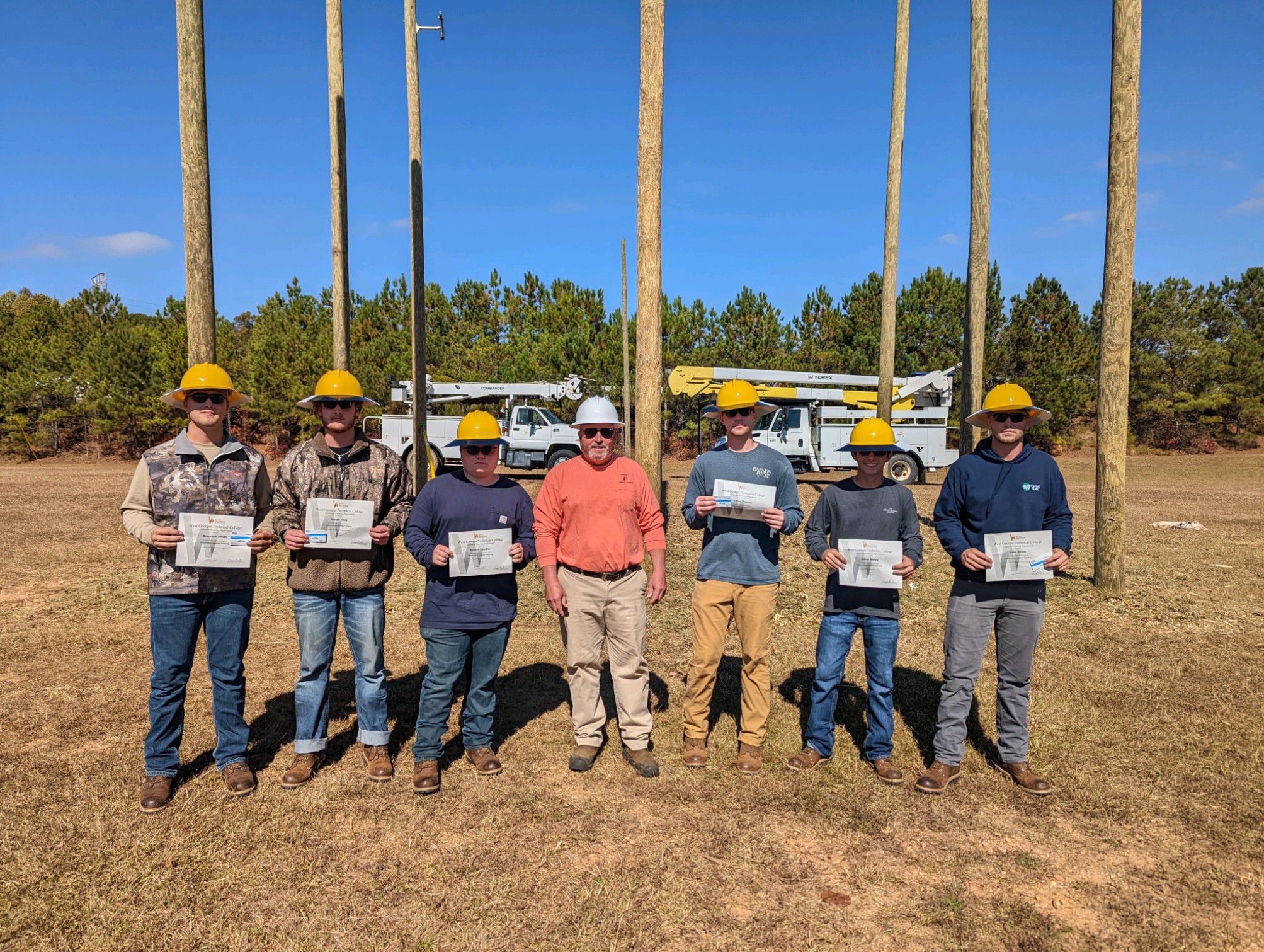 lineman graduates standing with certificates and hardhats