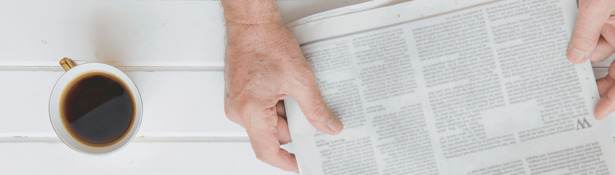 cup of coffee next to a person reading a newspaper